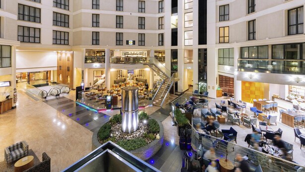 A multi-level hotel lobby with a central atrium, multiple dining areas, and a staircase.