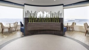 A reception area with a curved desk, seating, a cityscape wall, and a view of the sea.