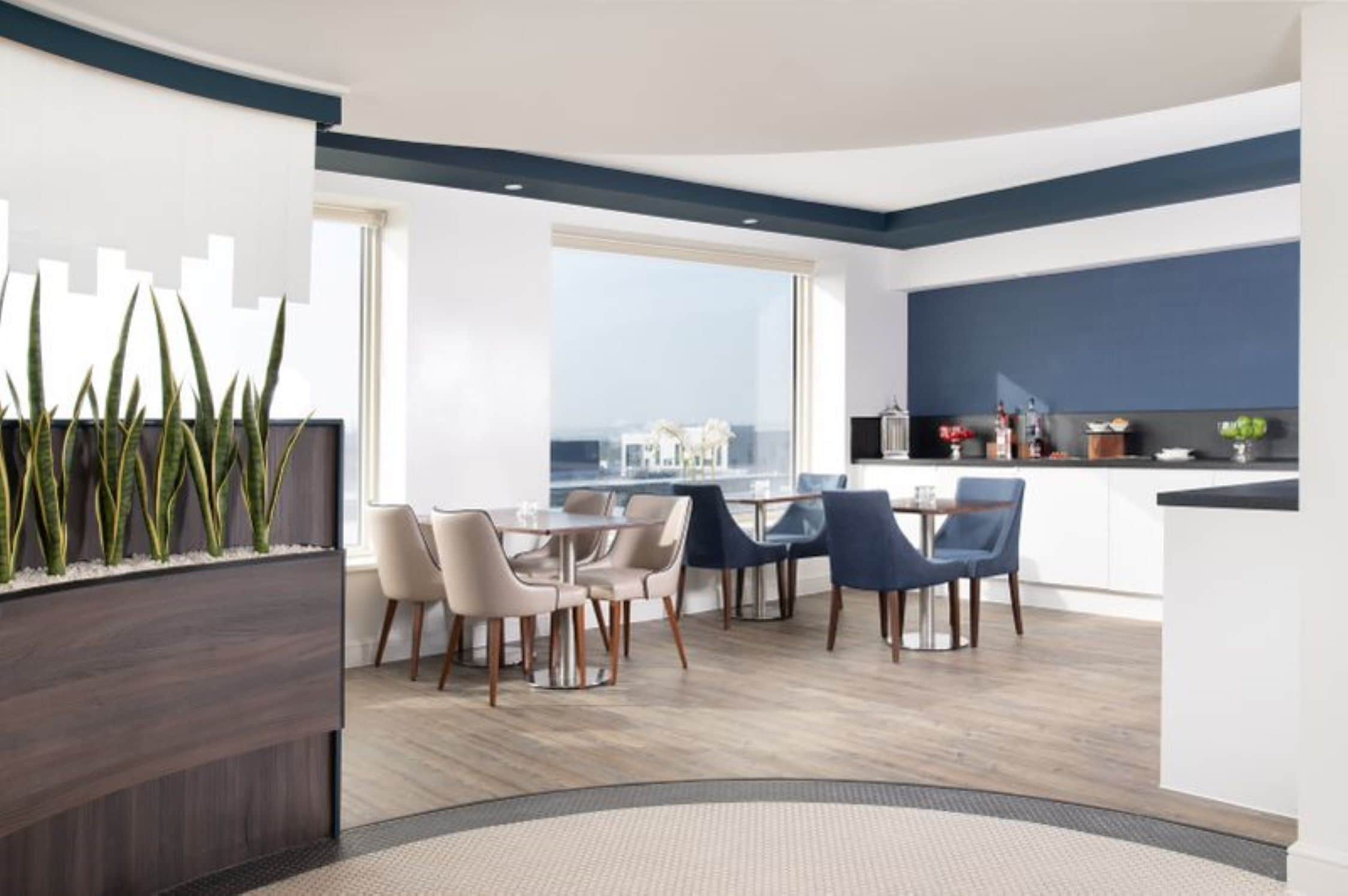 Un comedor moderno con vistas a la ciudad, una cocina con salpicadero oscuro y una disposición de asientos con una mezcla de sillas.