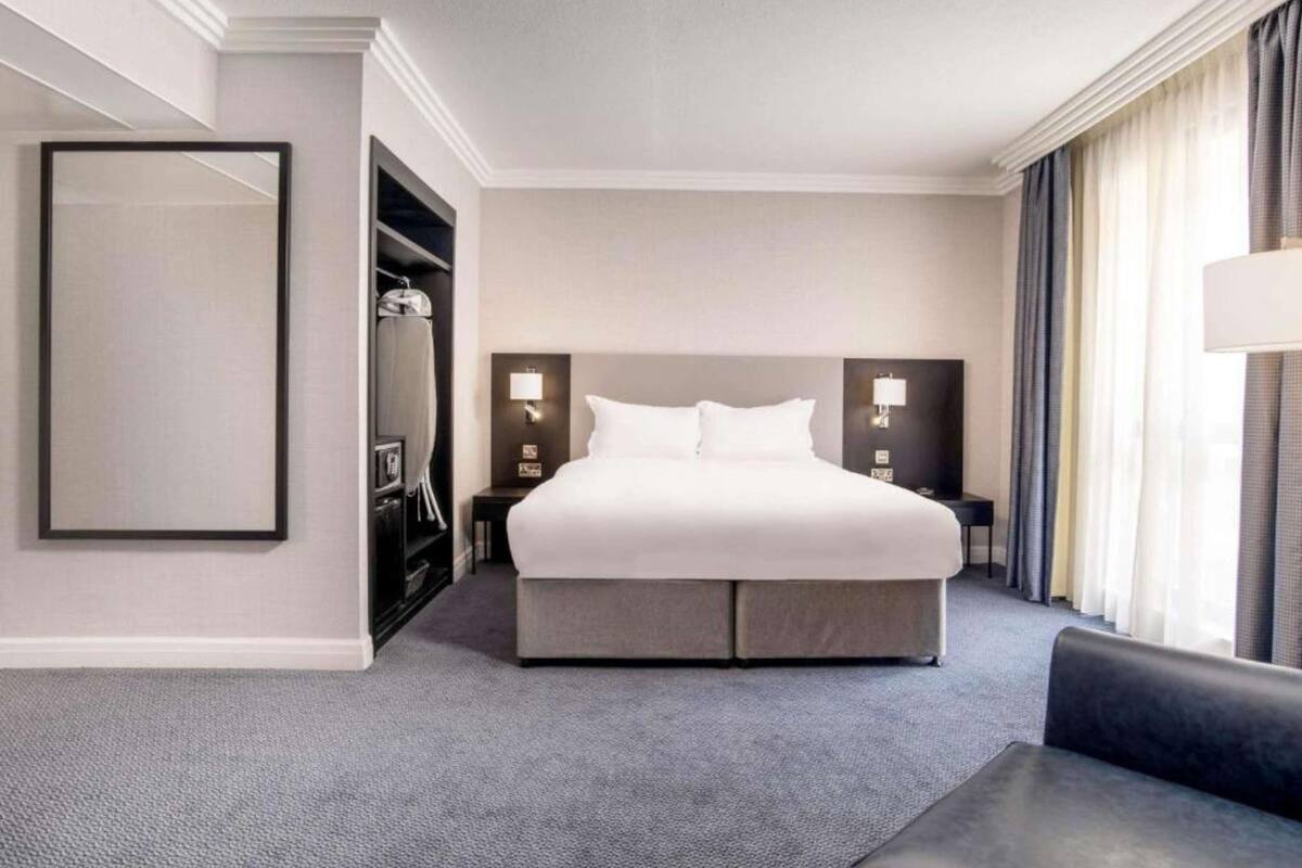 A hotel room with a large bed, a wardrobe, a bedside table, and a nightstand.