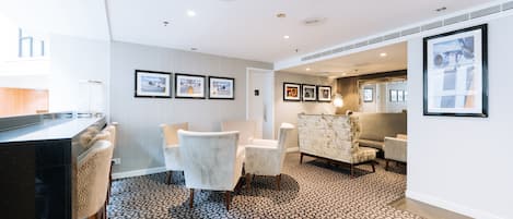 A hotel lobby with a reception desk, seating area with armchairs, framed pictures on the walls, and patterned carpet.
