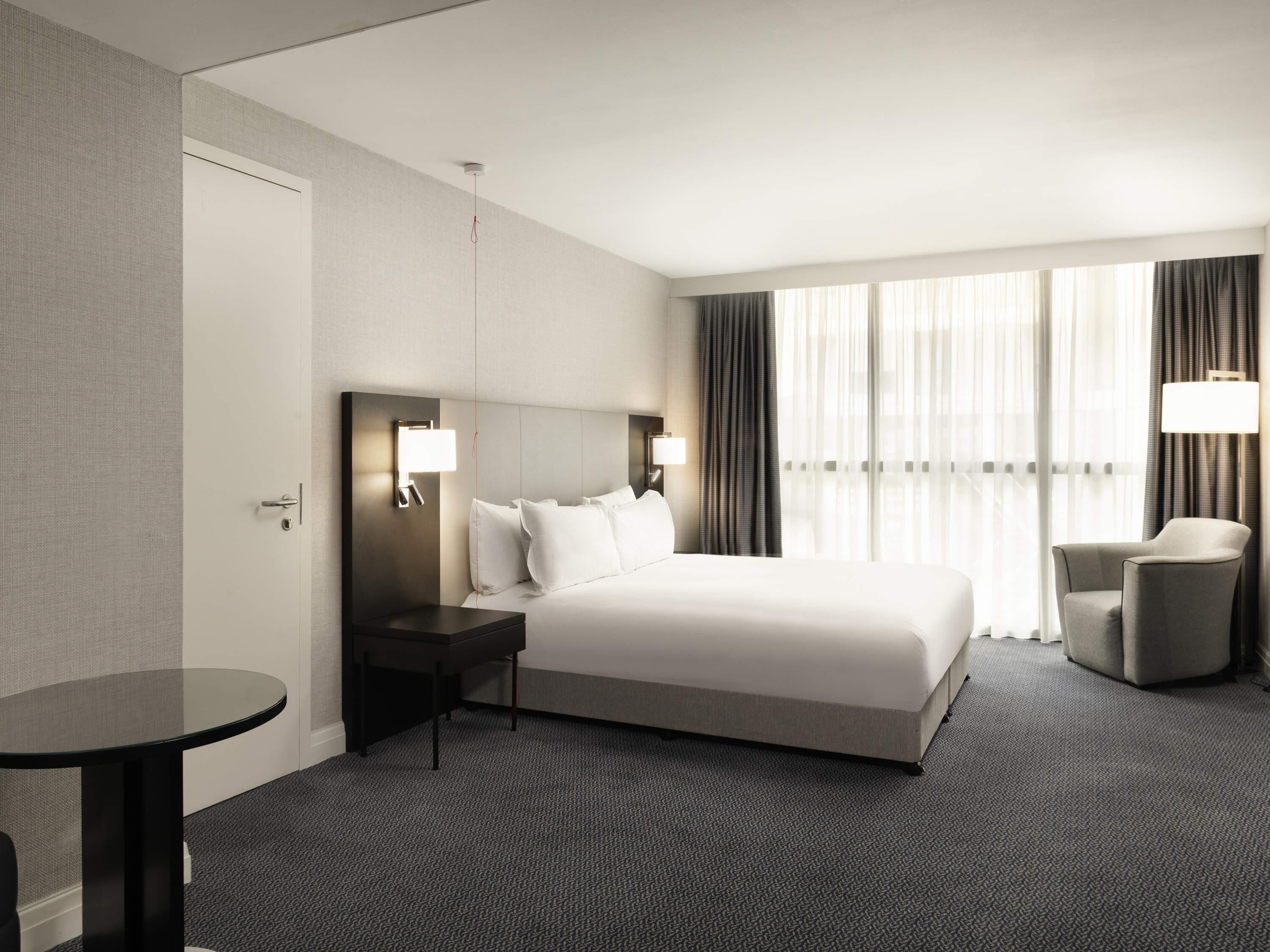 Una habitación de hotel con una cama grande, una mesita de noche, una silla y una pequeña mesa.