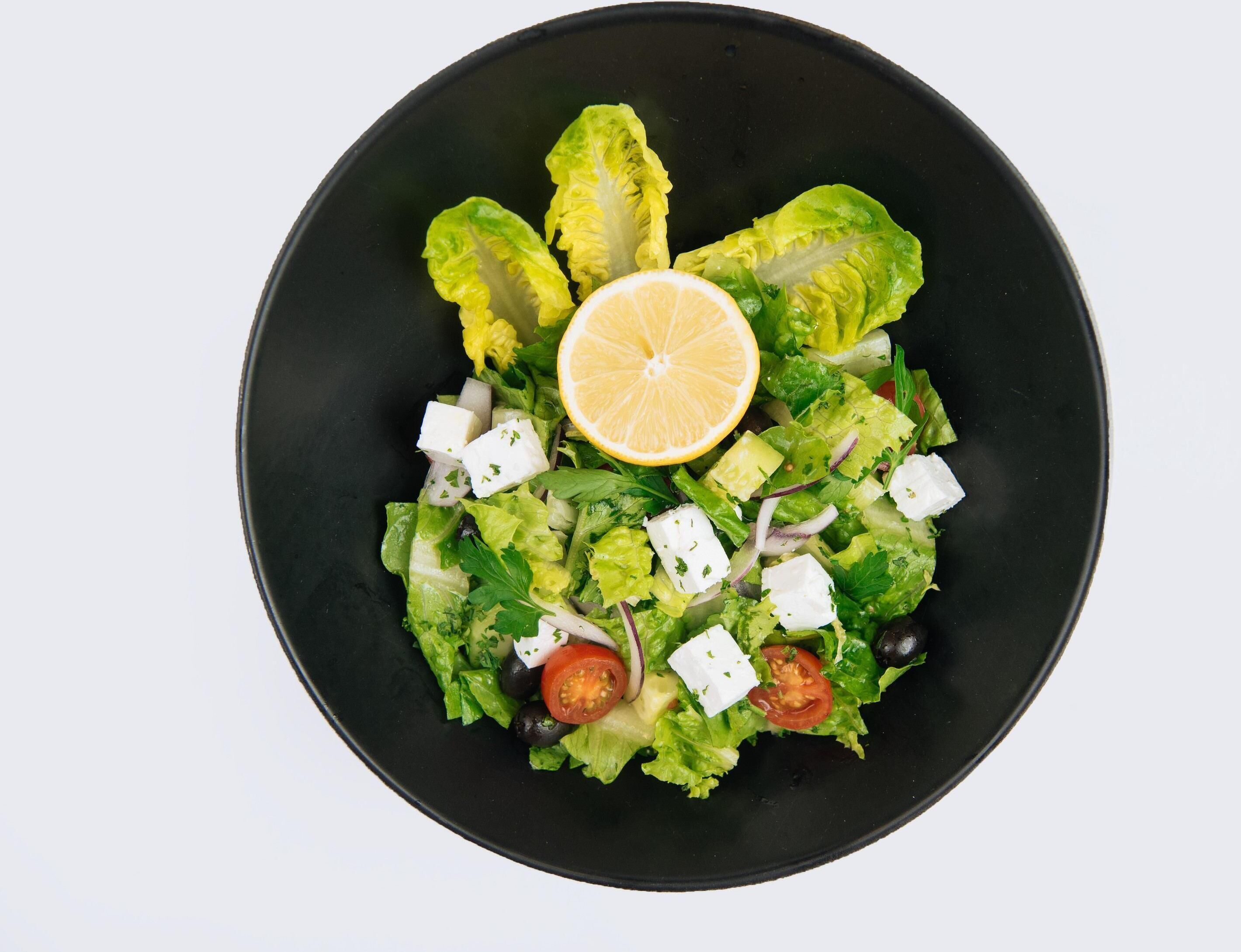 A salad with lettuce, tomatoes, black olives, and feta cheese on a black plate.