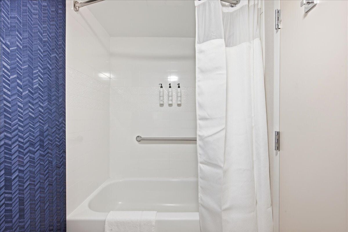 A bathroom with a shower, a towel rack, and a hand soap dispenser.