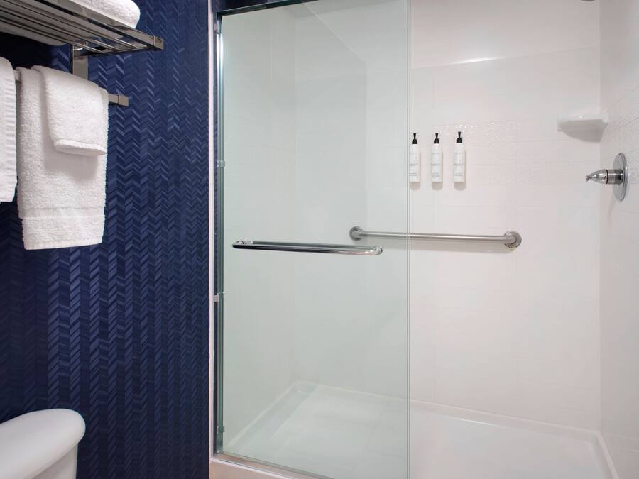 A modern bathroom with a glass shower enclosure, white tiles, and a blue patterned wall.
