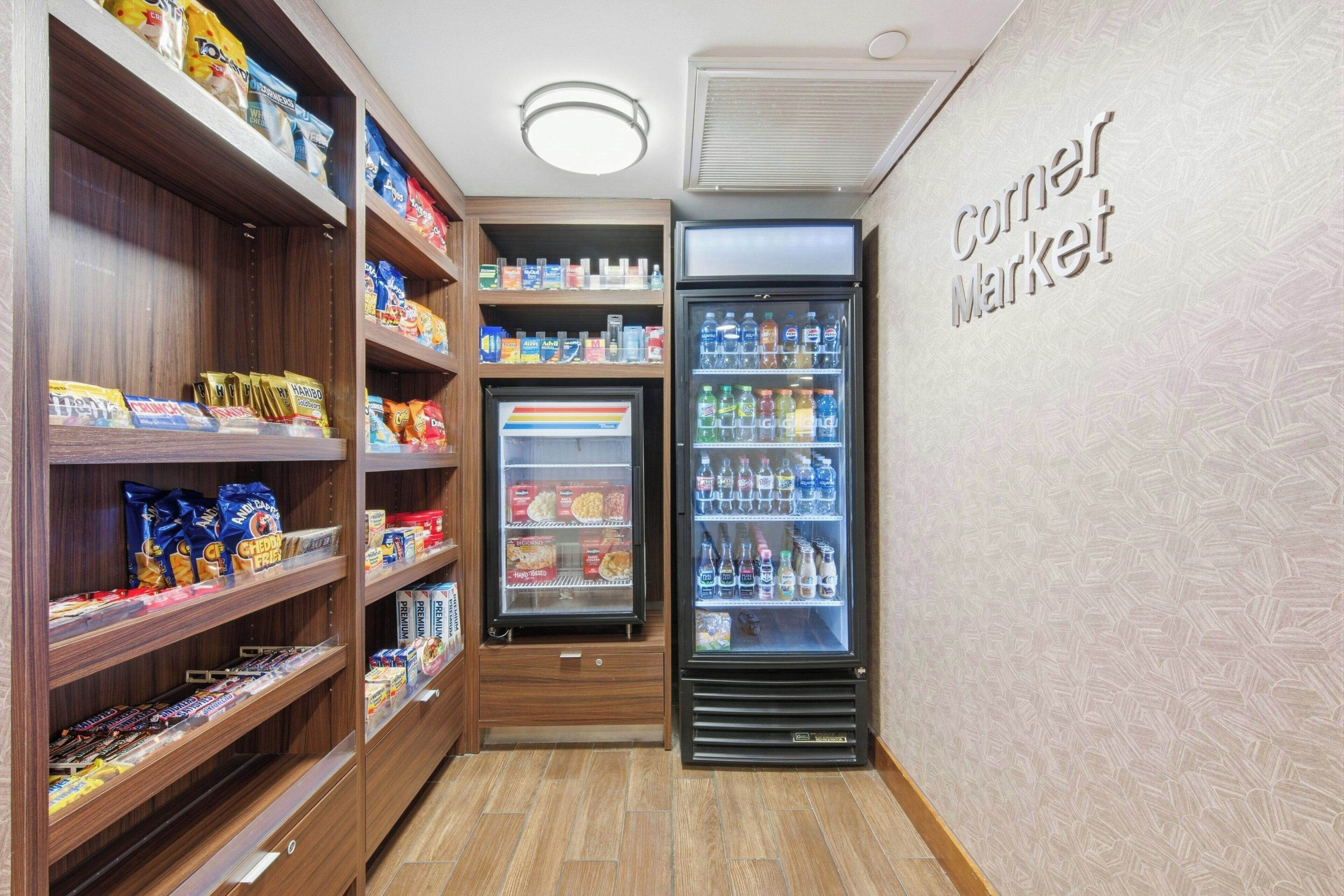 Une petite épicerie de quartier avec des étagères remplies d’en-cas et de boissons, un rayon réfrigéré et un panneau indiquant l’emplacement du magasin.