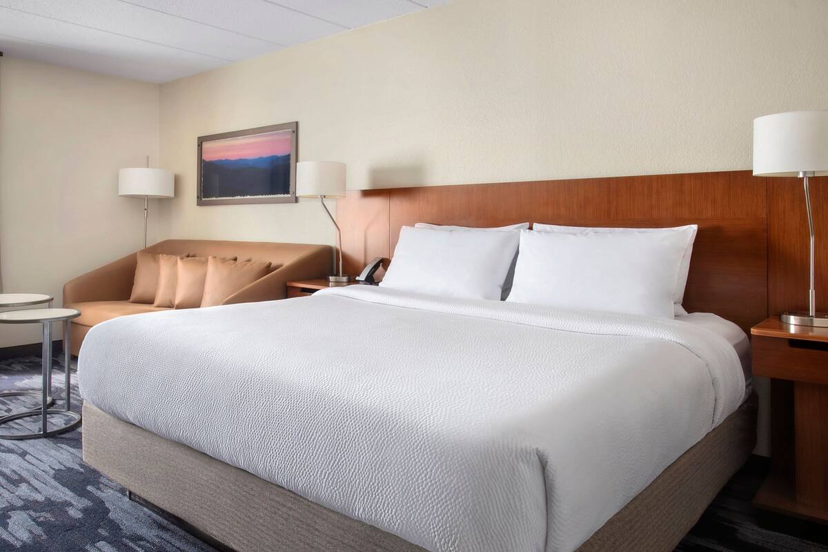 A hotel room with a large bed, a sofa, a desk, and a lamp.