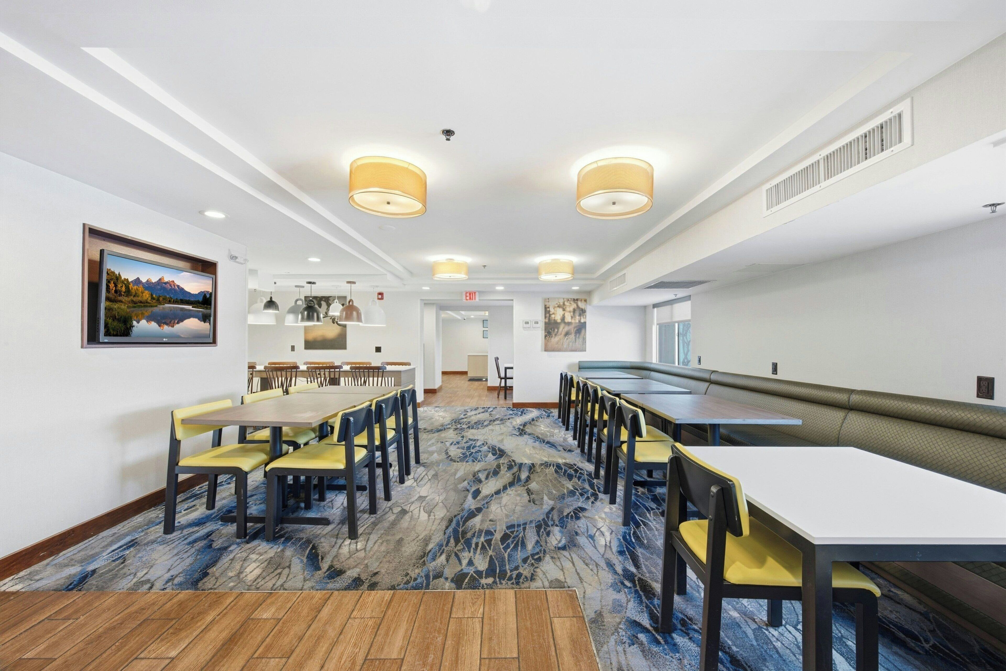 Een restaurantgedeelte in een hotel met een lange tafel, stoelen en een kamerbreed tapijt.