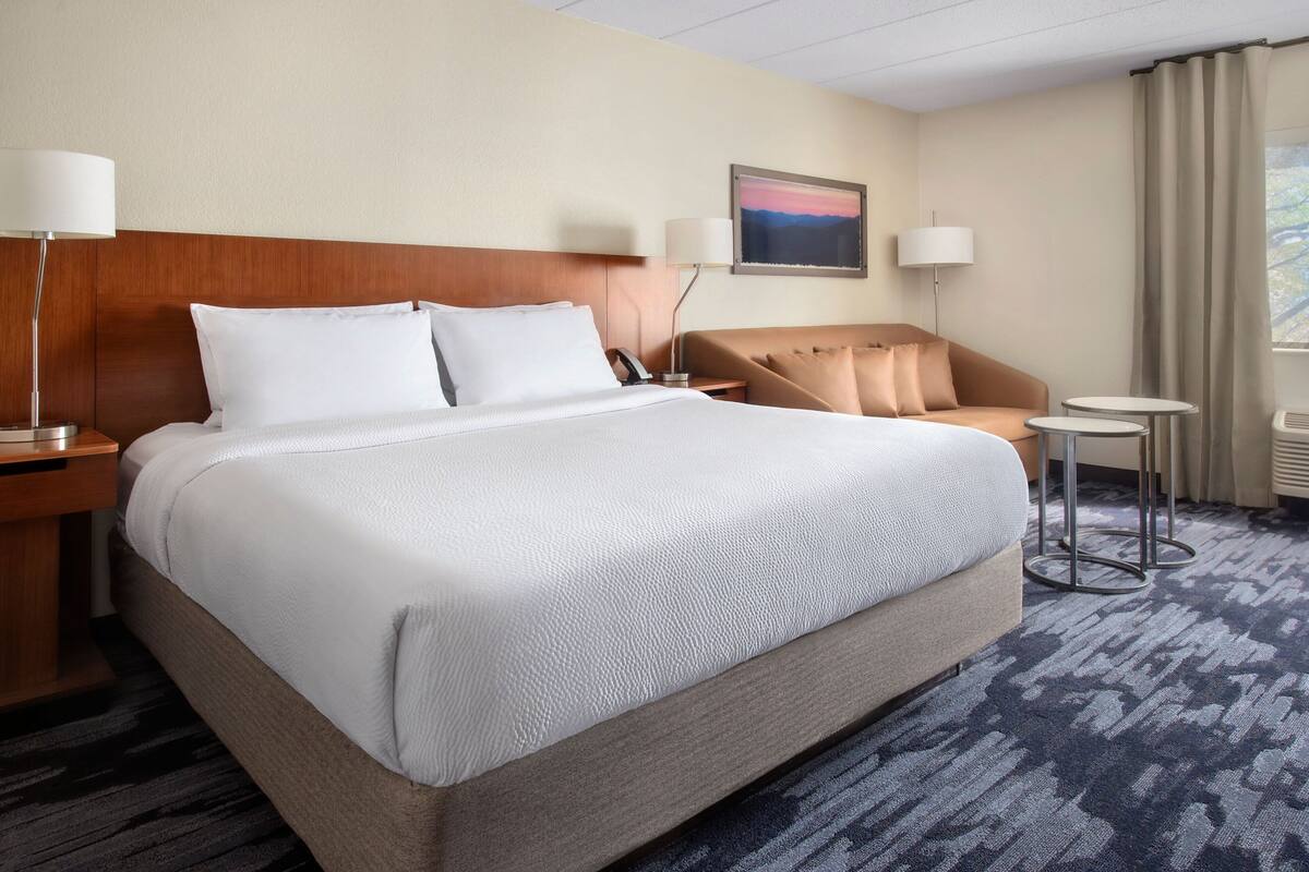 A hotel room with a large bed, two bedside tables, a chair, and a small table.