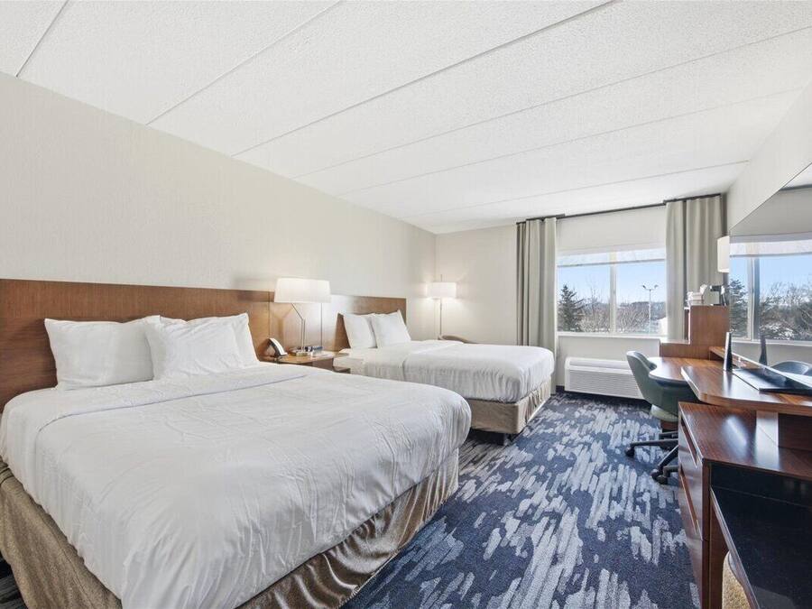 A hotel room with two beds, a desk, a chair, and a large window.