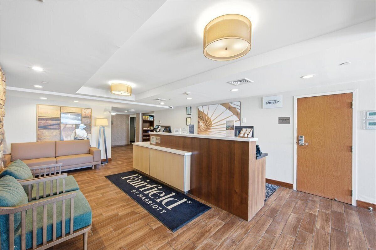 A hotel lobby with a reception desk, a sofa, a lamp, and a wooden floor.