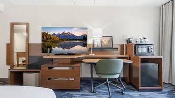 Ein Hotelzimmer mit einem Bett, einem Schreibtisch mit Computer, einem Fernseher, einer Lampe, einer Mikrowelle und einem kleinen Kühlschrank.