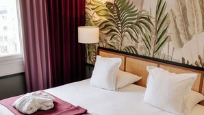 Habitación de hotel con una cama grande, cortinas rojas, almohadas blancas y un mural temático de la selva tropical.