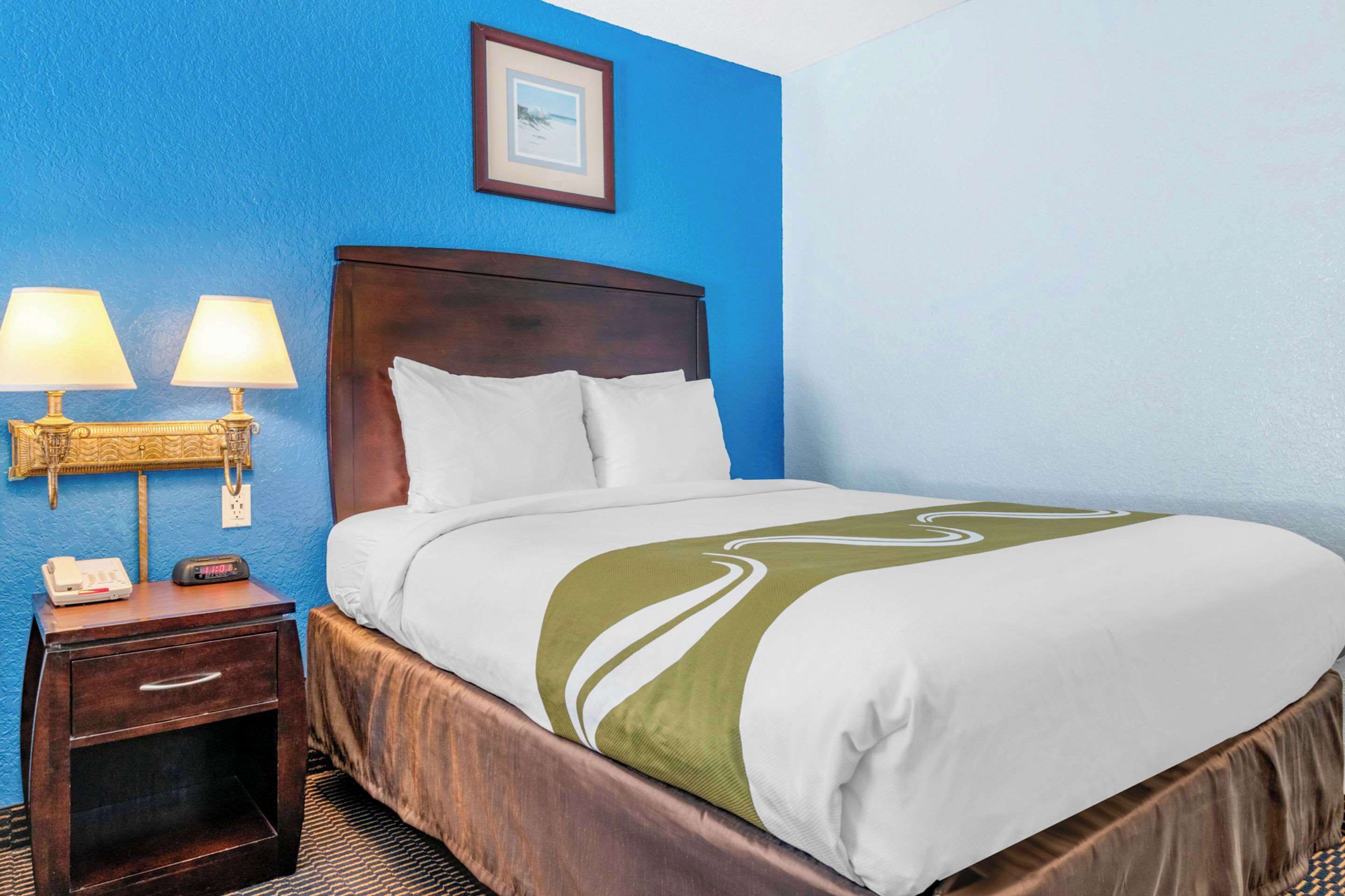 Una camera d'albergo con un letto, un comodino, lampade e un quadro appeso al muro.