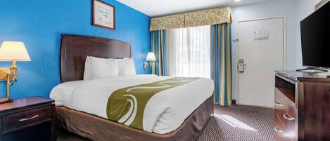 Una habitación de hotel con una cama grande, una mesita de noche con lámpara, un aparador y un televisor.