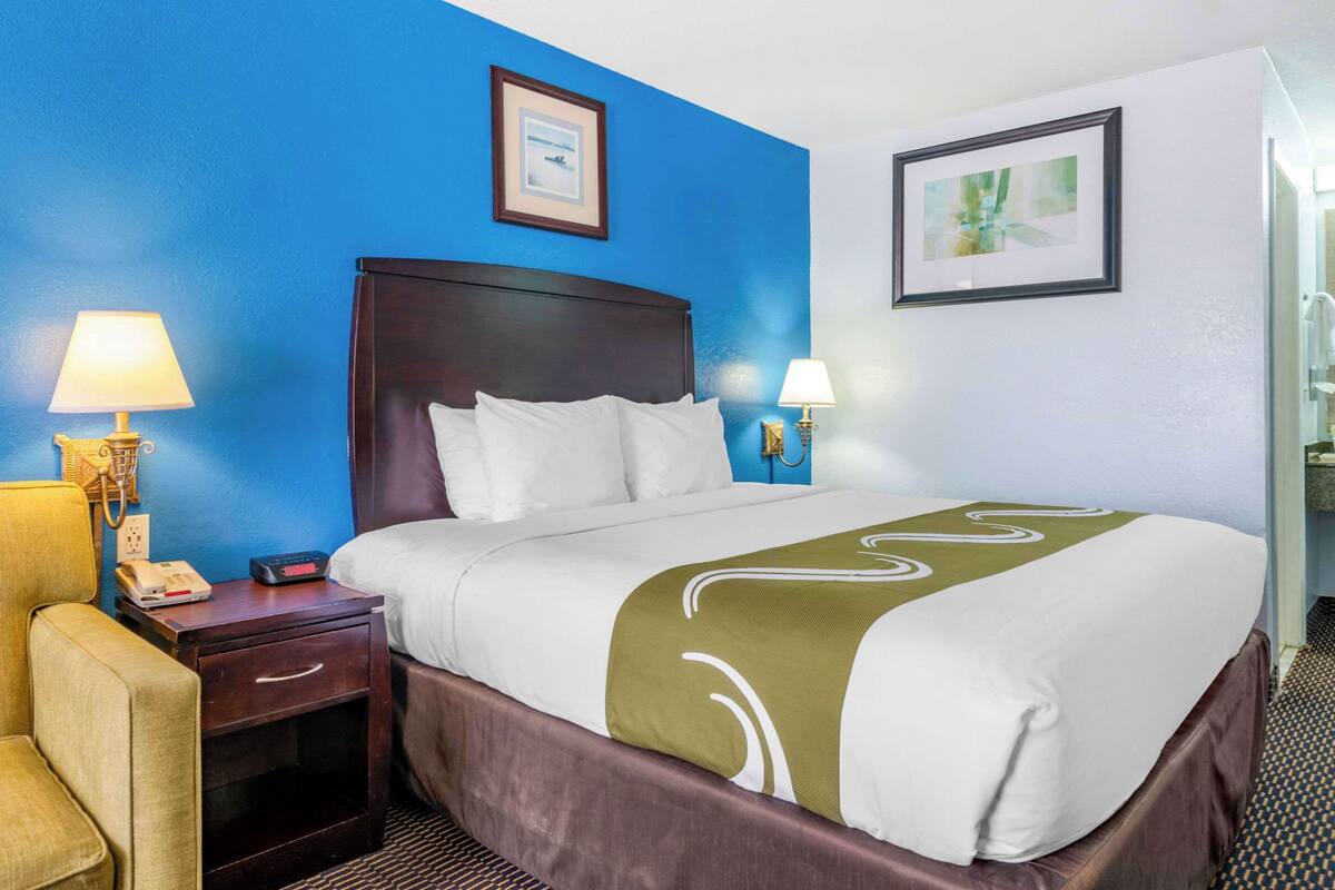 A hotel room with a large bed, two bedside tables with lamps, a chair, and a framed picture on the wall.
