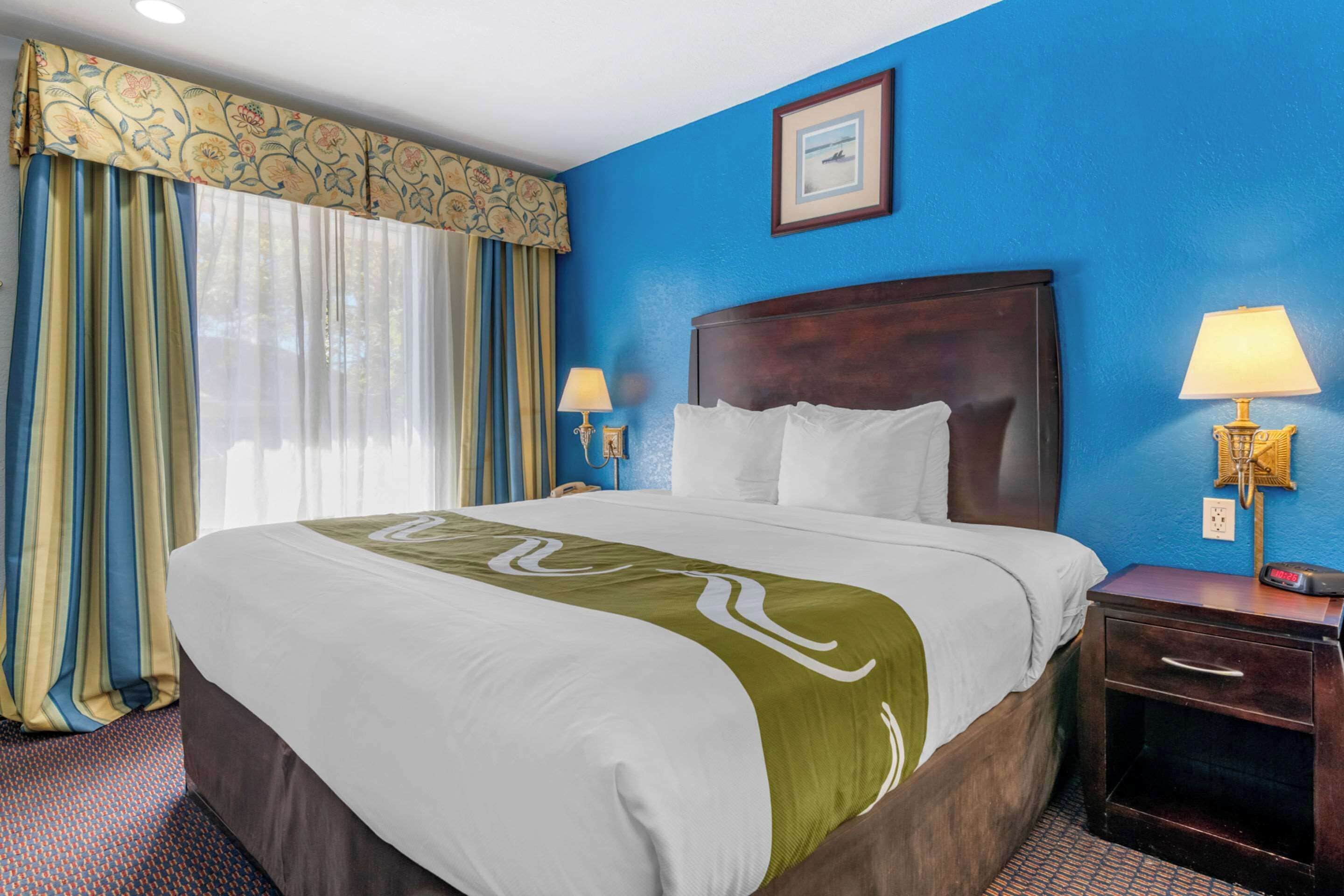 A hotel room with a large bed, two bedside lamps, a nightstand, and a window with curtains.
