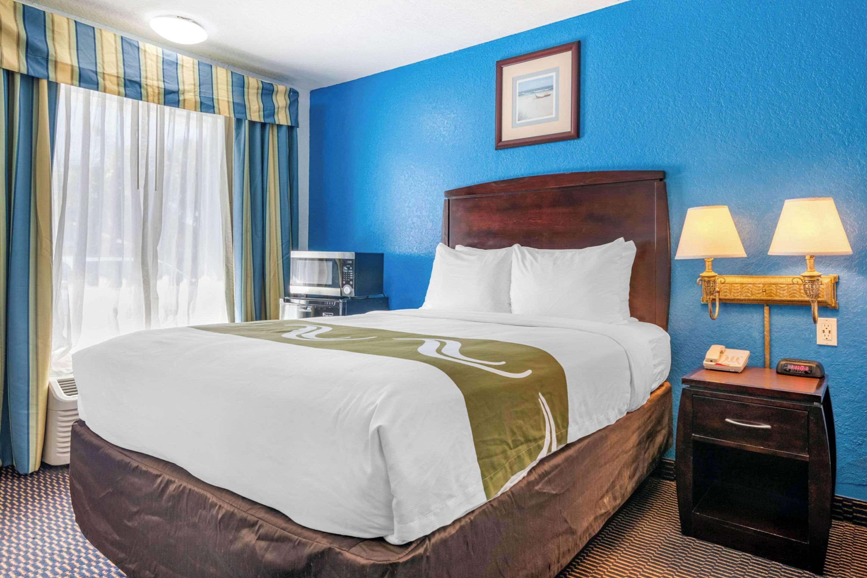 A hotel room with a large bed, a bedside table with lamps, a clock, and a picture on the wall.