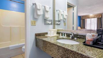 A bathroom with a granite countertop, white sink, and a large mirror. There are towels hanging on a rack and a shower visible in the background.