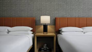 Habitación de hotel con dos camas, una mesita de noche con lámpara y un papel tapiz estampado.