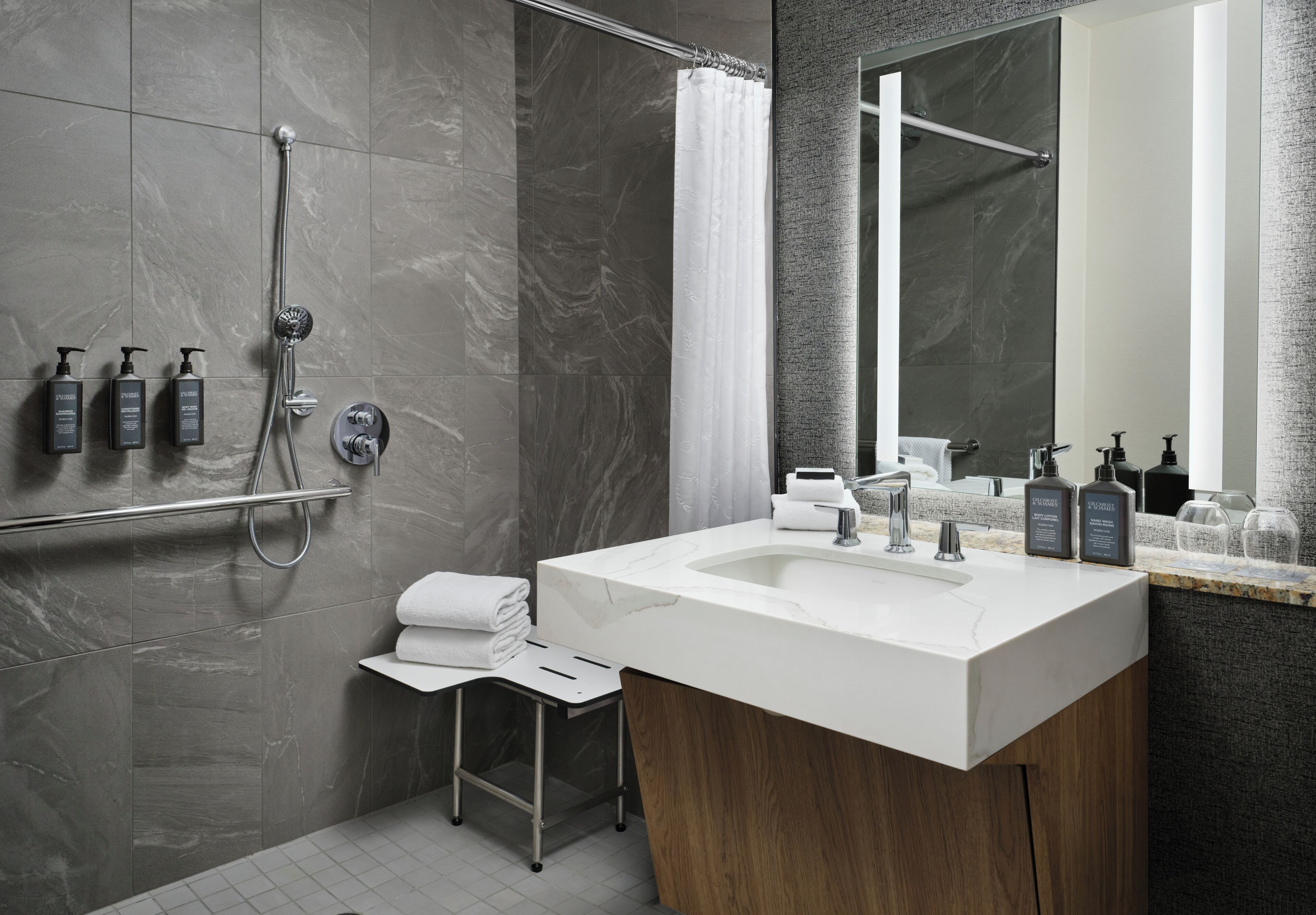 A modern bathroom with a large sink, a shower with a handheld showerhead, and a vanity with a mirror.