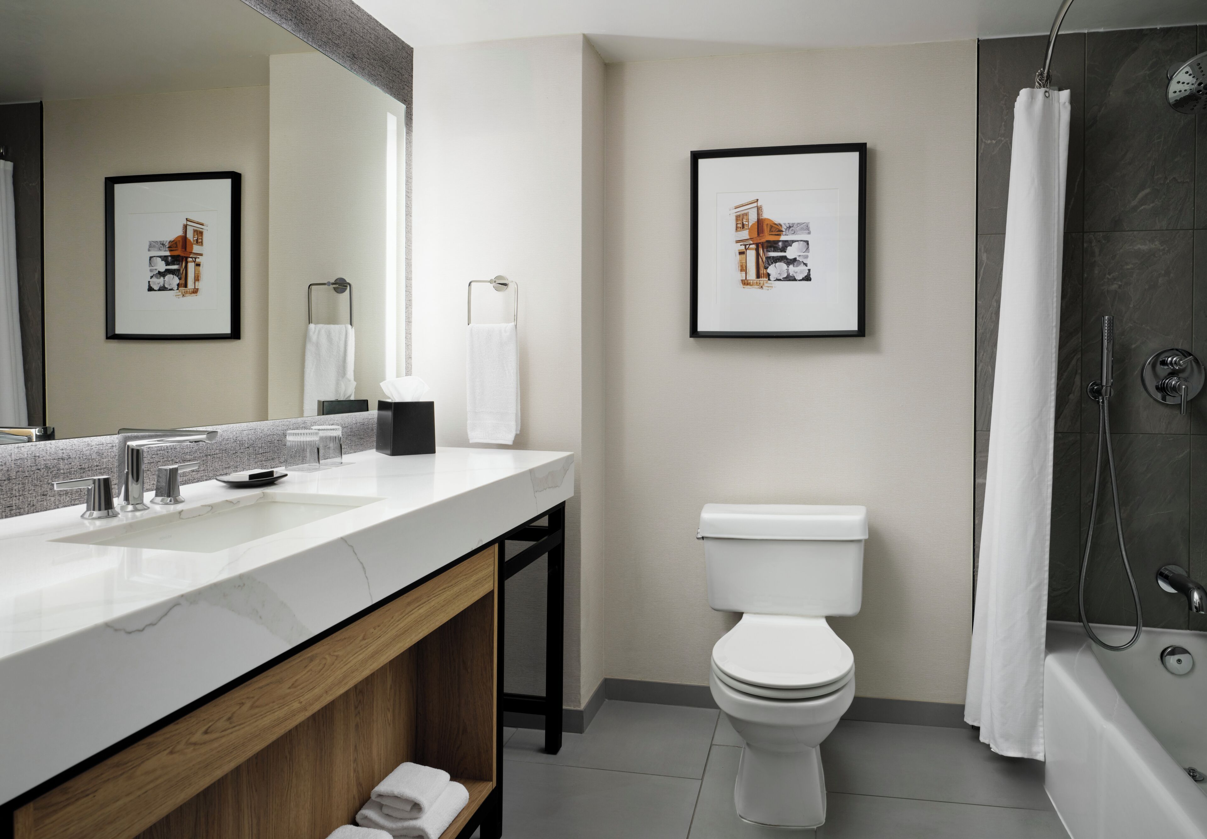 Une salle de bain moderne avec un lavabo blanc, des toilettes et une douche. Des tableaux encadrés ornent le mur.