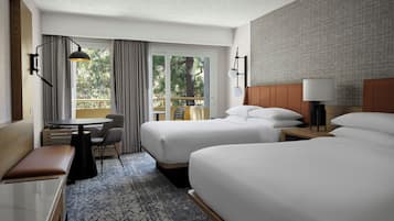 A hotel room with two beds, a desk, a chair, a small table, and a window with curtains.
