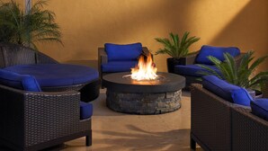 A patio area with wicker furniture, a stone fire pit, and potted plants.