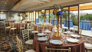 A banquet hall with round tables set for dining, gold chairs, and floral centerpieces.