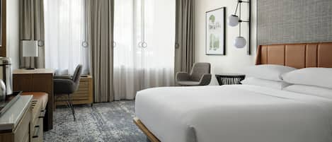 A hotel room with a large bed, a desk, a chair, a small table, and a wall-mounted lamp.