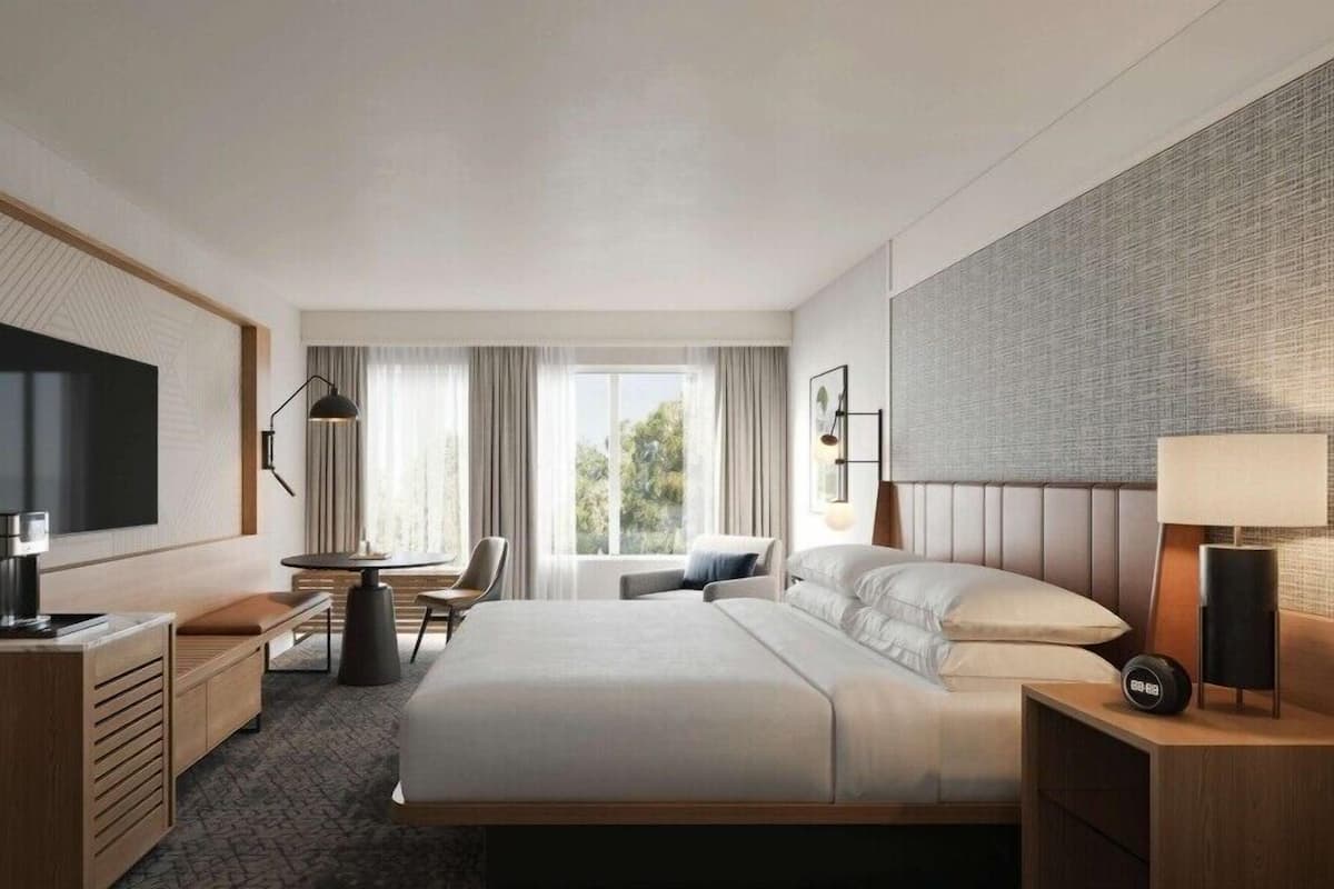 A modern hotel room with a large bed, a desk, a chair, a TV, and a window with curtains.
