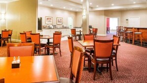 Een restaurantgedeelte in een hotel met meerdere tafels en stoelen, een keuken op de achtergrond en een kamerbreed tapijt.