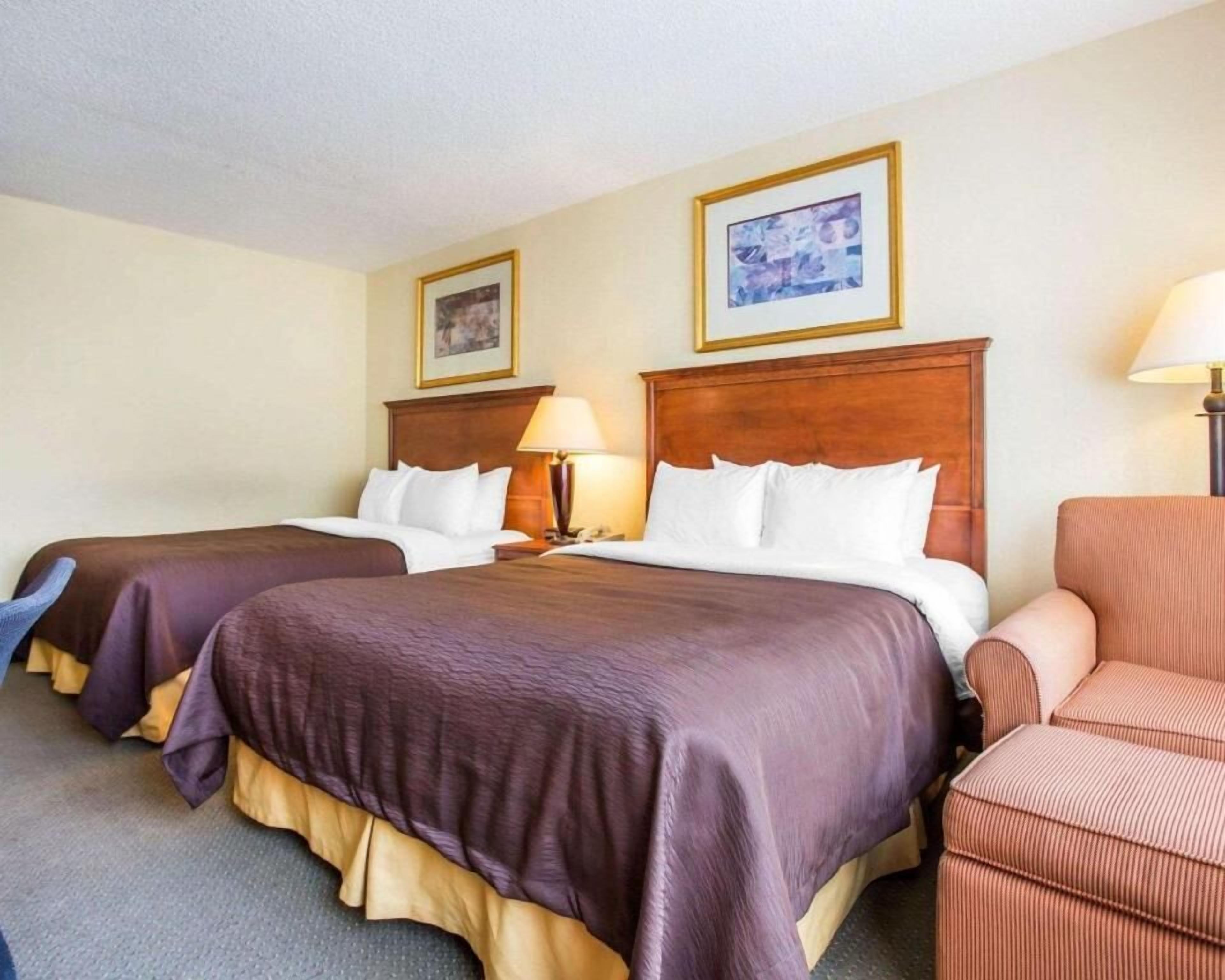 Una habitación de hotel con dos camas, un cabecero de madera, una silla y una lámpara.