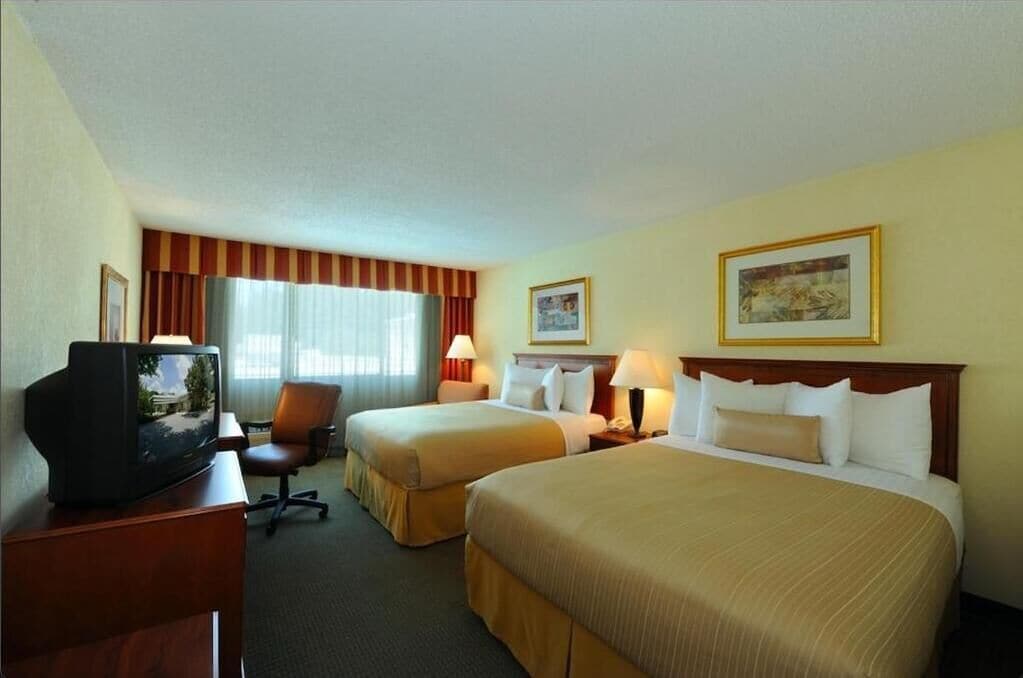 Een hotelkamer met twee bedden, een bureau met een televisie en twee lampen.