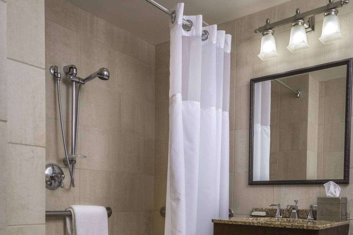 A bathroom with a shower, a sink, a mirror, and a towel rack.
