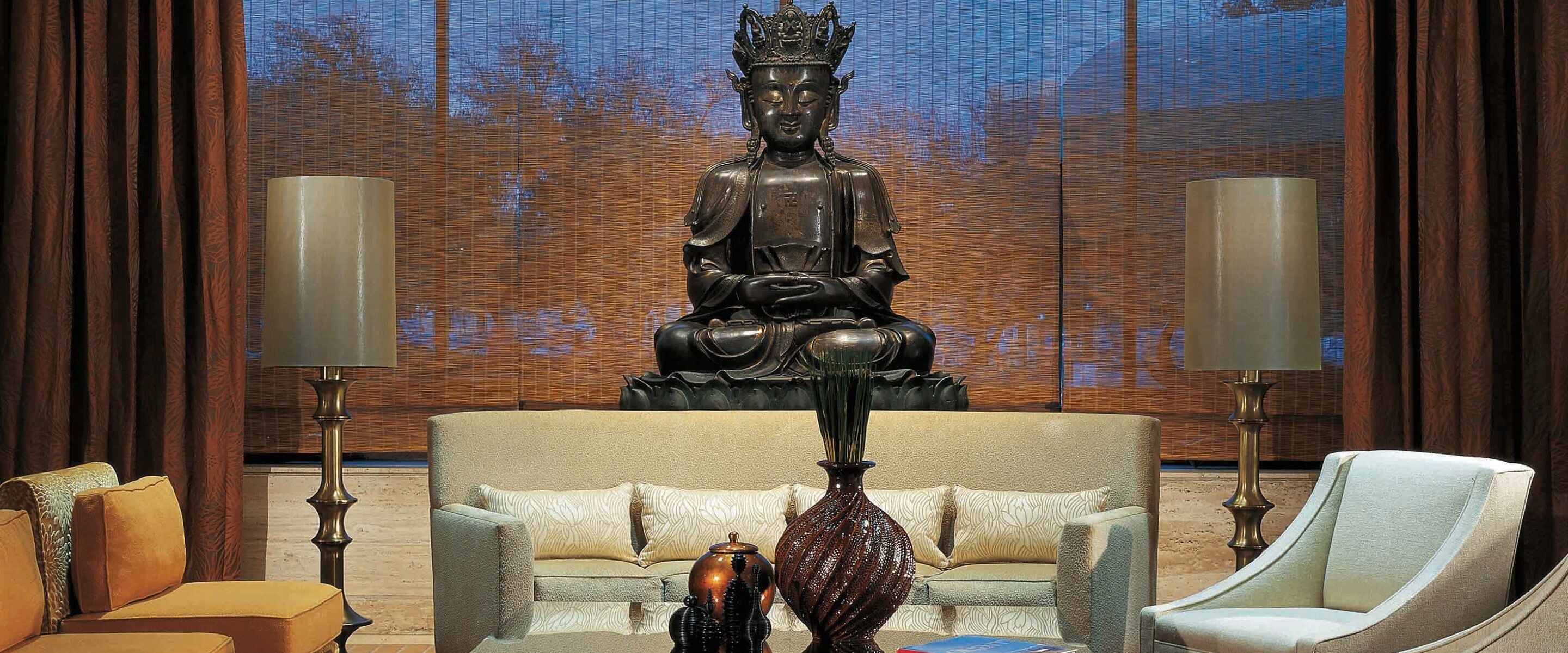Una habitación con una gran estatua de Buda, dos lámparas, un sofá y una silla.