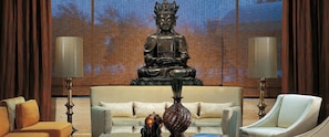A room with a large Buddha statue, two lamps, a sofa, and a chair.