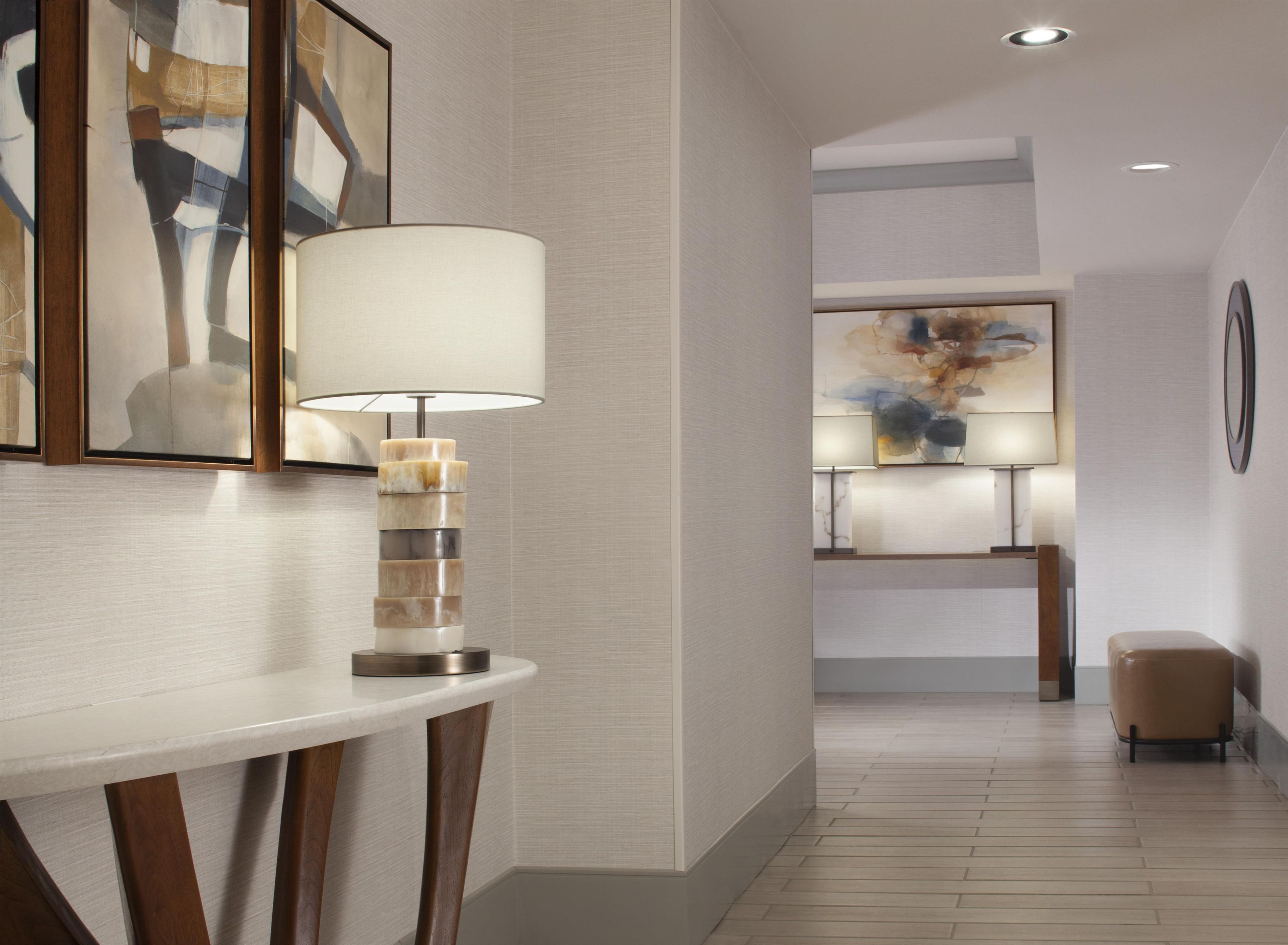 A modern hotel lobby with a white reception desk, a unique multi-tiered lamp, and abstract wall art.