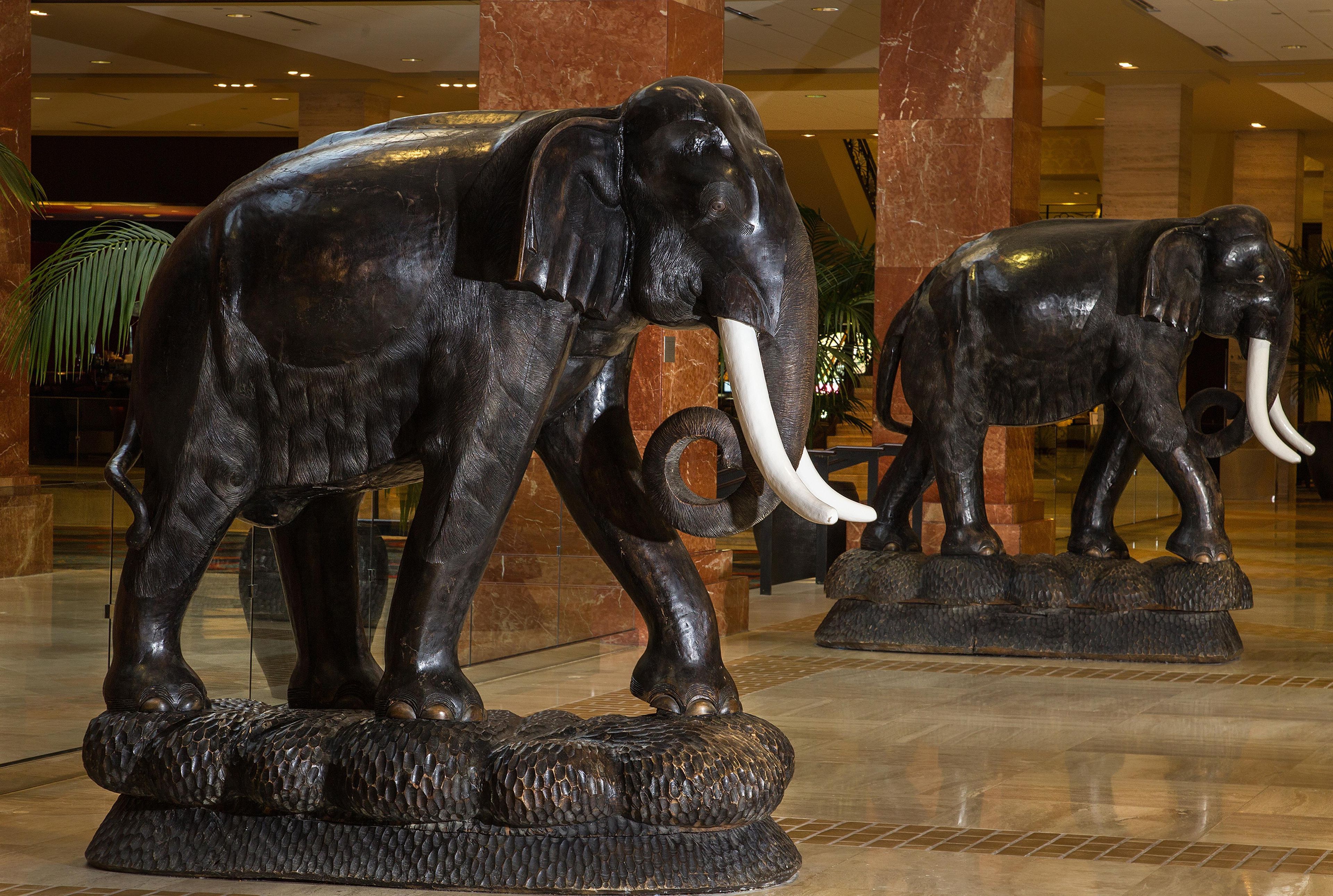 Zwei Elefantenstatuen auf Podesten in einer Lobby mit Marmorsäulen und gefliestem Boden.