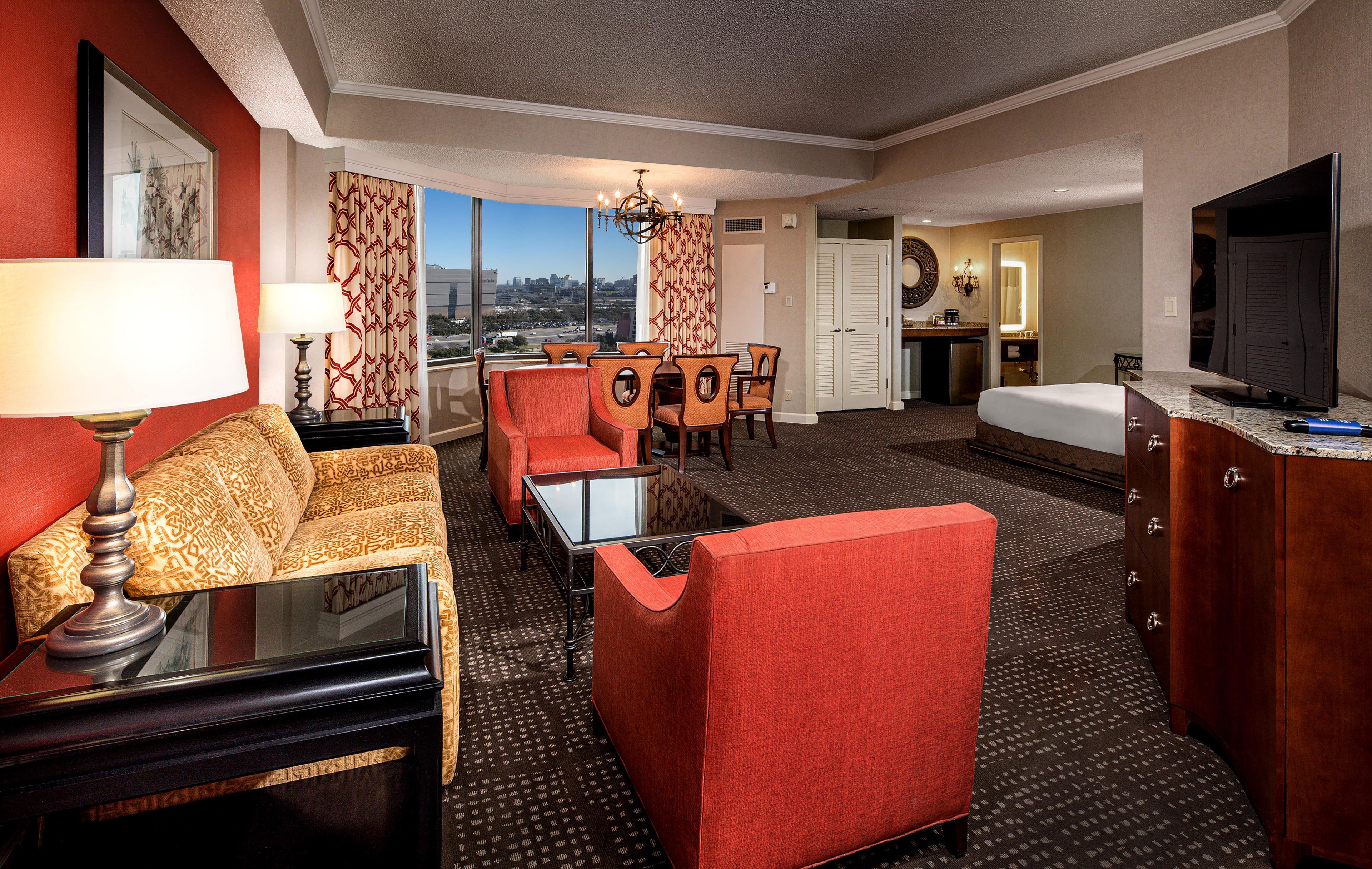A hotel room with a bed, a desk, a chair, a sofa, a television, and a view of the city.