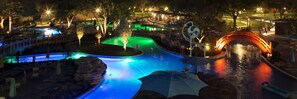 A nighttime swimming pool area with a bridge, seating, and a signpost.