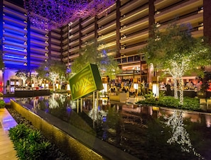 A modern indoor atrium with a reflective water feature, seating areas, and a large illuminated sign.