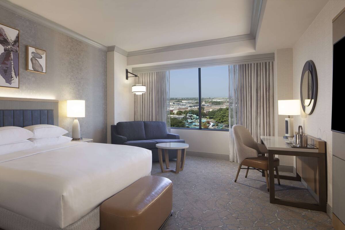 A hotel room with a large bed, a sofa, a desk, and a view of a cityscape.