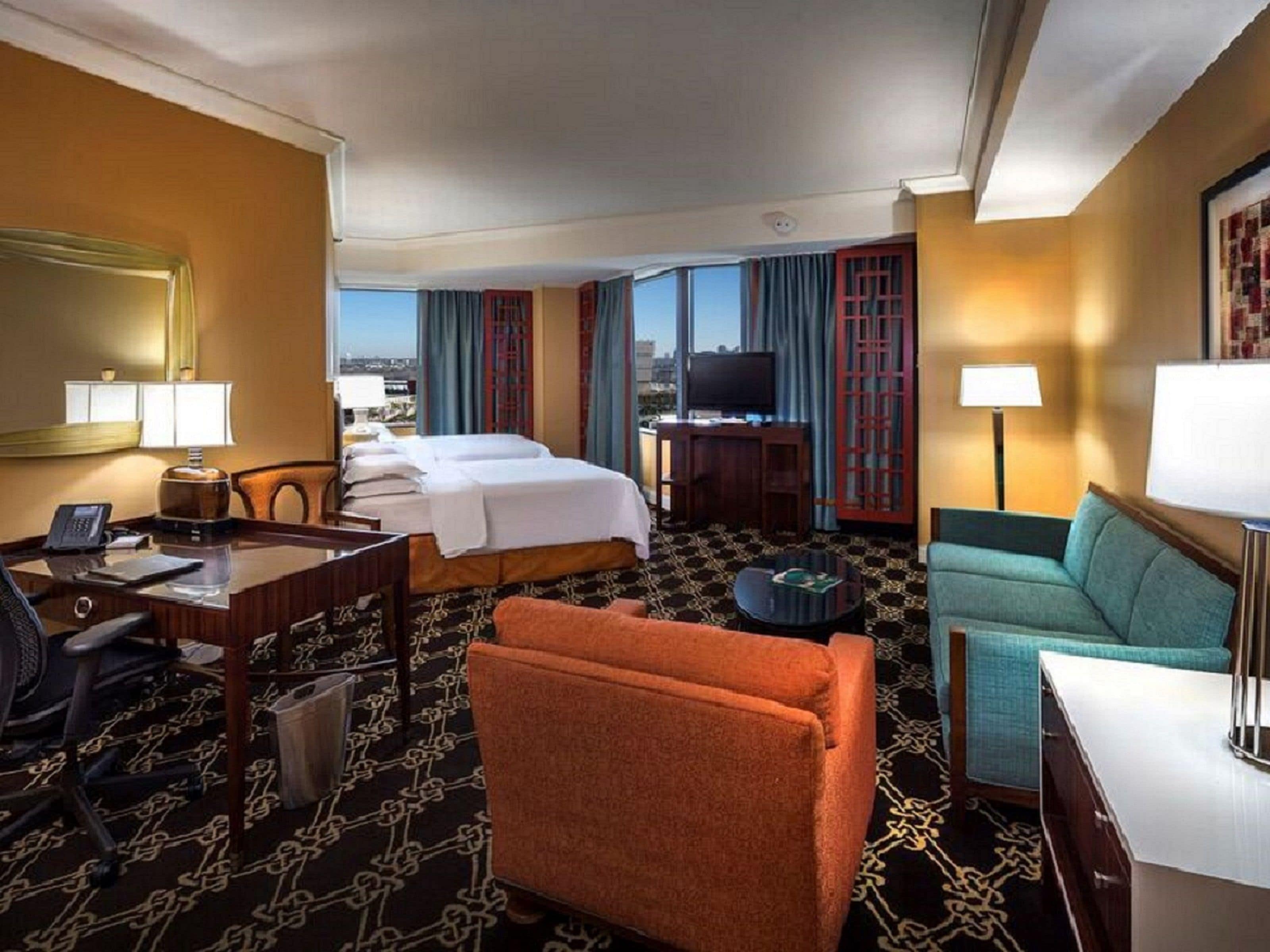 A hotel room with two beds, a desk, a sofa, a television, and a city view.