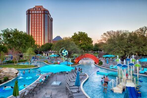 A hotel pool area with a water slide, lounge chairs, and a tall building in the background.