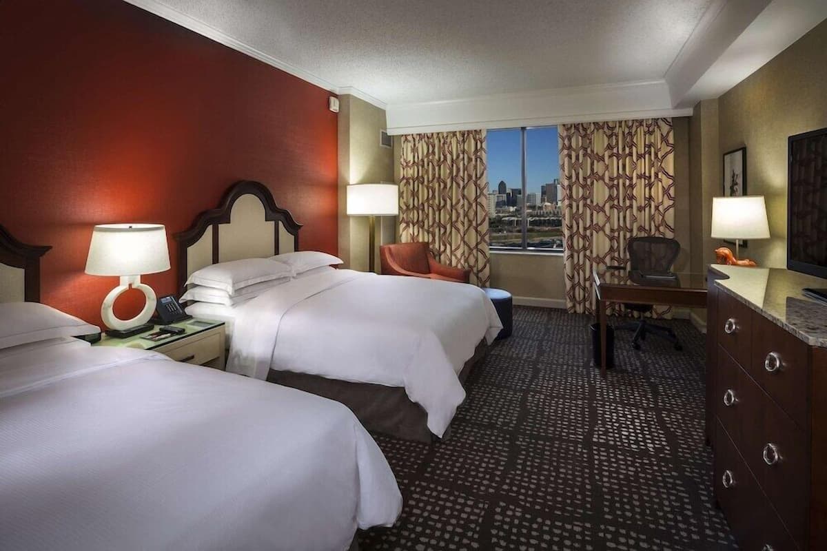 Une chambre d’hôtel avec deux lits, un bureau, une chaise et une vue sur la ville.