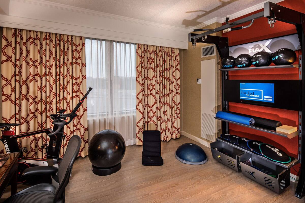 A home gym with exercise equipment, including an elliptical, a stationary bike, a punching bag, and a weight bench.
