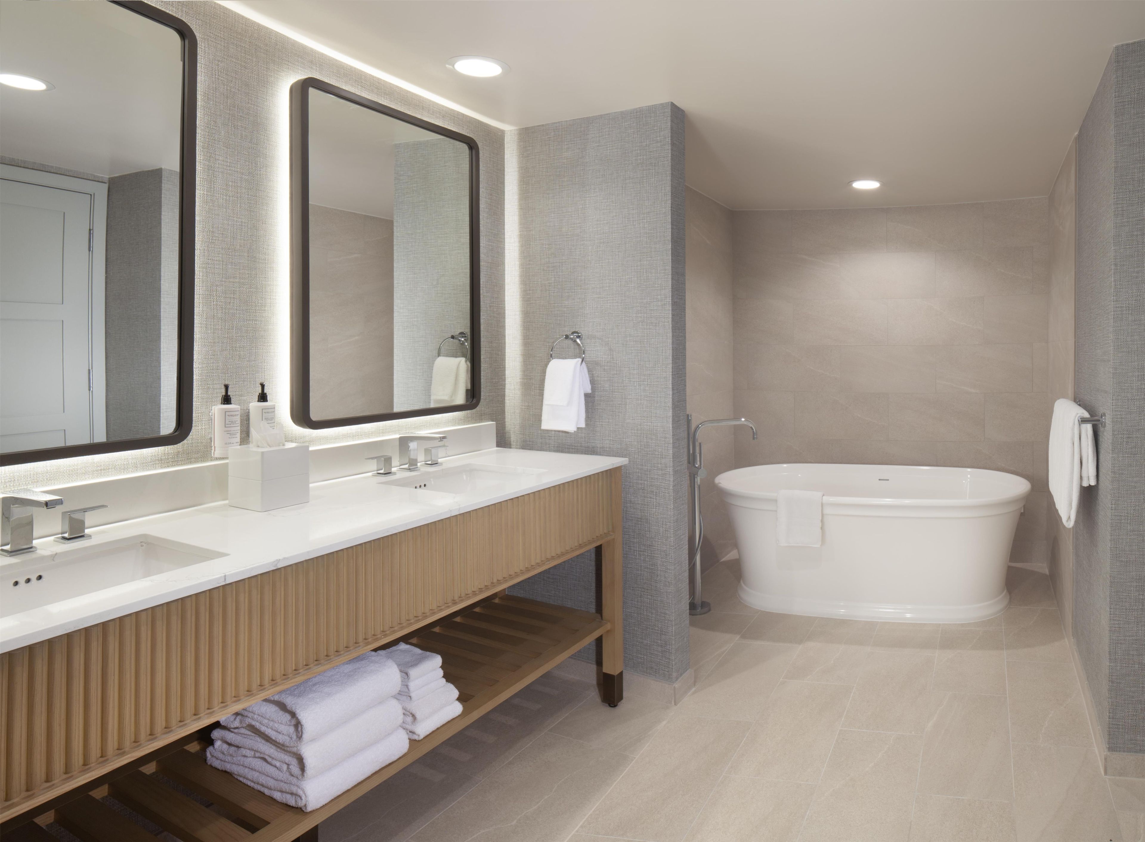 A modern bathroom with a double sink vanity, a large mirror, a bathtub, and a towel rack.