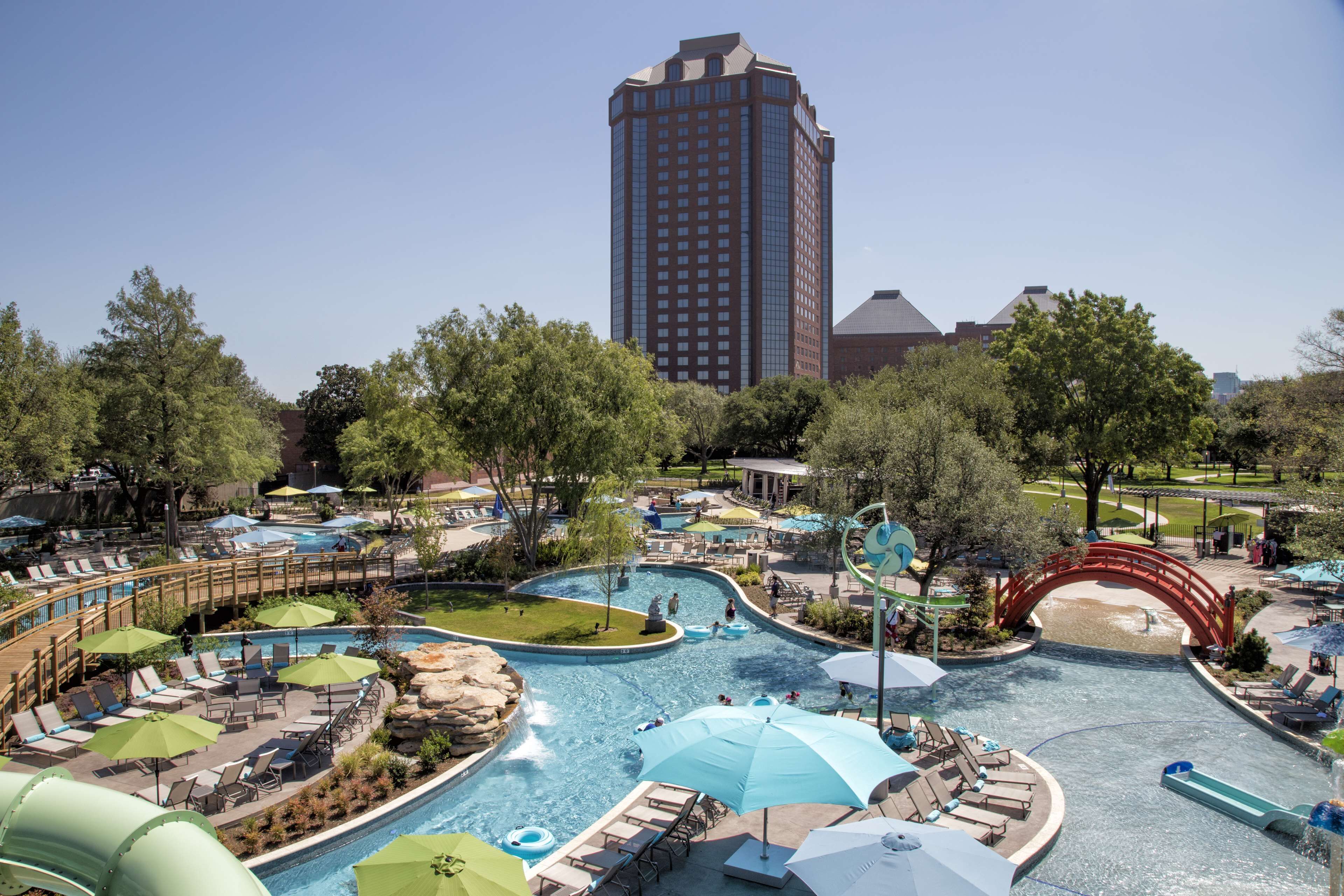 Un resort con una gran piscina, zonas de descanso y un edificio alto al fondo.