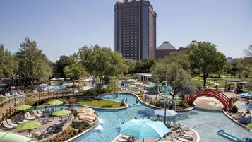 Un resort con una gran piscina, zonas de descanso y un edificio alto al fondo.